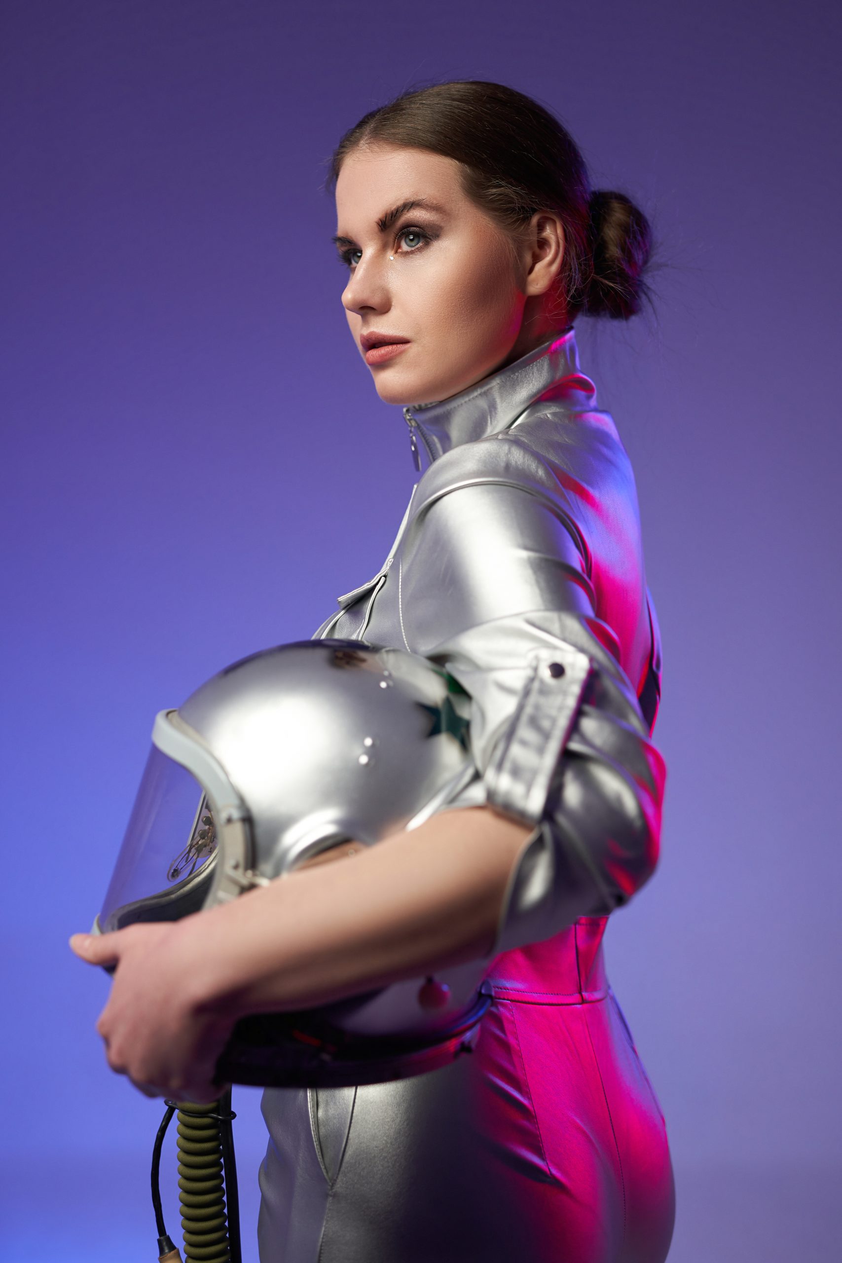 Studio shot of woman astronaut in silver protective uniform holding helmet.